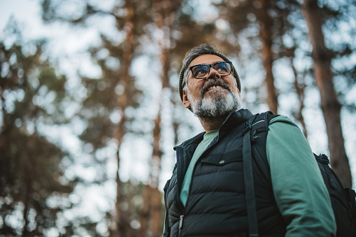 Portrait of mature man with backpack and camera hiking and taking photos in nature.