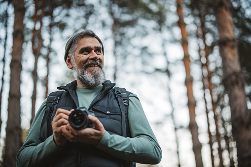 Portrait of mature man with backpack and camera hiking and taking photos in nature.