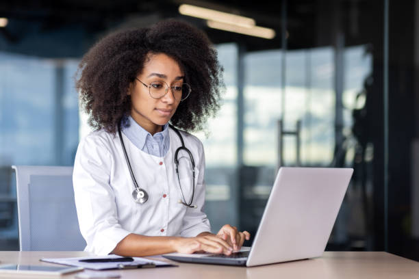 istock African american female therapist dressed in uniform typing on laptop while sitting at workplace in hospital. Pretty physician using modern device and internet for helping and supporting patients 2033779354