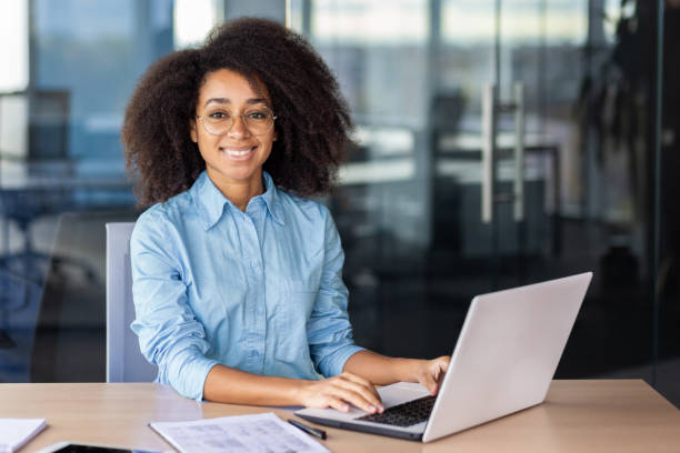 istock Cheerful diverse woman smiling at camera while keeping hands on portable computer keyboard in workplace. Remote digital designer feeling satisfied with completing massive high paying task online 2033835303