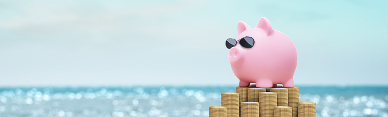 pink piggy bank on the beach with glasses on a stack of coins - summer vacation savings concept