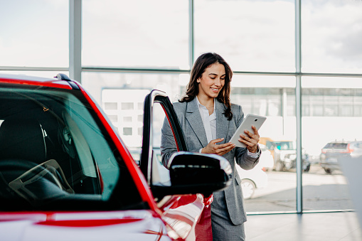 Showcasing a tech-savvy approach, a woman in the showroom uses a digital tablet to enhance her car shopping experience, blending technology with traditional browsing