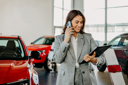 Amidst the gleaming cars, a woman is caught in a moment of conversation on her phone in the showroom, her discussion echoing the busy world of automotive decisions and connections
