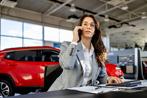 Amid the sleek cars of the showroom, a woman's attention to detail shines as she finalizes administration tasks, ensuring every document is in order for a seamless transaction