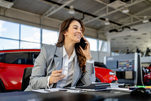 In a car showroom, a woman's confidence is evident as she finalizes the paperwork, sealing deals that bring joy and new vehicles to satisfied customers