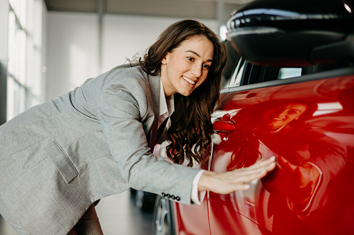 In the showroom, a woman embracing her new car is a powerful image of automotive dreams turned reality, her affectionate gesture signifying a bond that goes beyond the mechanical