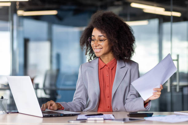 istock Confident businesswoman in modern office working on laptop holding documents 2033890480