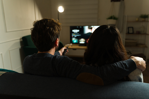 Rear view of a married couple relaxing on the couch and watching tv streaming services in the living room