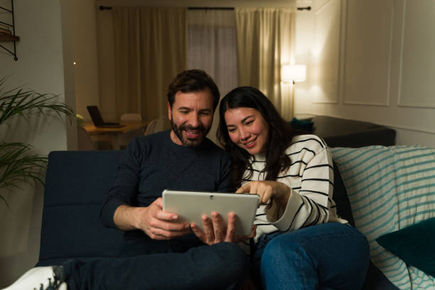 istock Smiling couple enjoying while relaxing on the couch using the tablet 2033925427