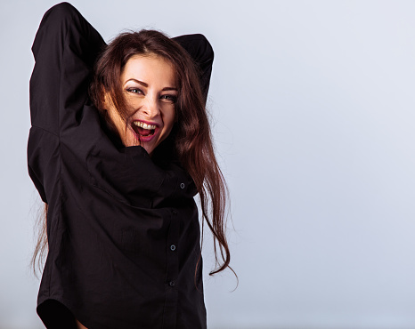 Enjoying happy toothy laughing and positive crying woman posing in black shirt standing with brown hair on studio blue background with empty copy space. Closeup front classic banner portrait