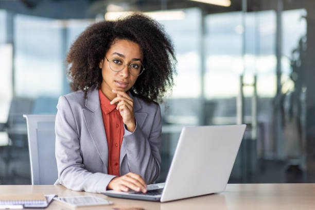 istock Thoughtful latino person resting head on chin while working by portable computer next to tablet and notebook. Pensive female boss making choice which employee deserving promotion to leading position 2033939034