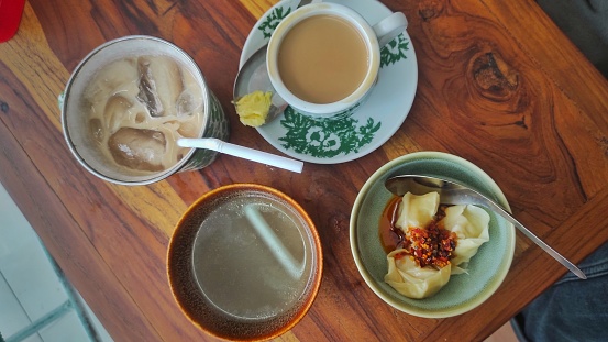 Iced milky tea, butter coffee, and dumplings with chilli souce and broth served on the wooden table