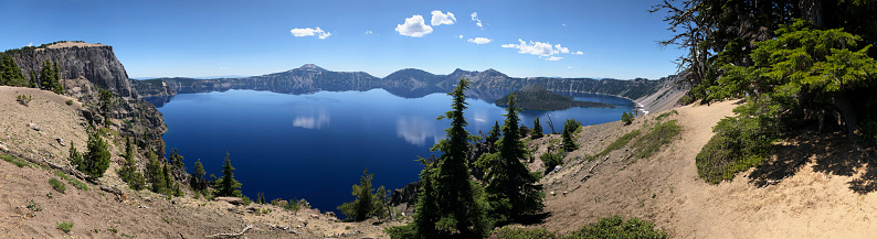 Crater Lake panorama photo taken in summertime on a sunny day with a few clouds in the sky