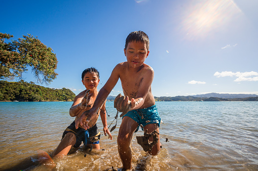 Kids playing with sand at Puriri Bay, Whangaruru North Head, Bay of Islands, Northland New Zealand.