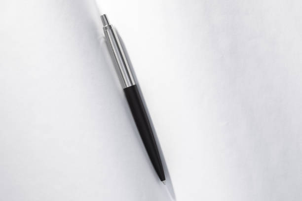A ballpoint pen rests on top of a stack of documents ready for signing. The image is photographed using a very shallow depth of field with the focus being on the tip of the pen.