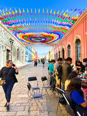 Oaxaca, Mexico: Folk artists at work on a colorful street in downtown Oaxaca as a woman walks by; the street is decorated with papel picado—the Mexican art of cut paper.