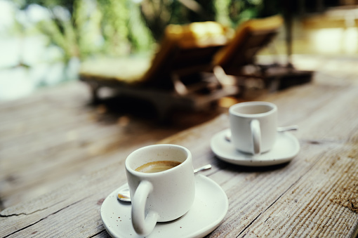A cup of coffee rests on a primitive wooden table against the backdrop of lush tropical island scenery. Sunlight filters through, casting warm rays onto the surface of the coffee, releasing its enticing aroma. This serene corner invites one to embrace the tranquility of nature, as if time slows down in this moment. Captured with the Leica Q3.