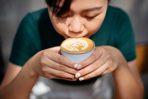 Young Asian woman drinking cafe latte in a cafe. Morning coffee routine or coffee break concept.