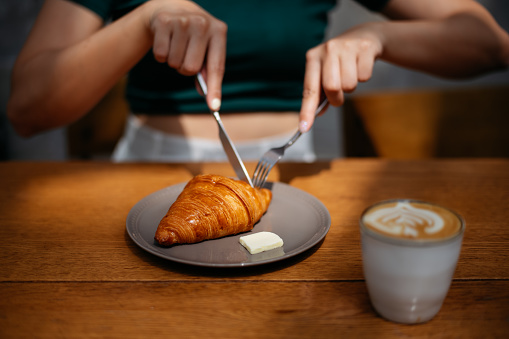 Close up shot of an Asian woman having croissant and coffee in a cafe