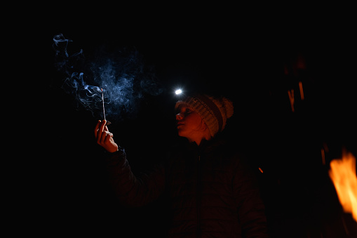 A young girl holds a stick that is burning and she makes smoke patterns.