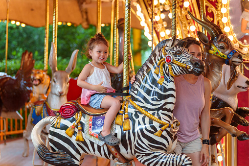 An adorable three year old Eurasian girl of Hawaiian and Chinese descent smiles with excitement as she rides on a carousel.
