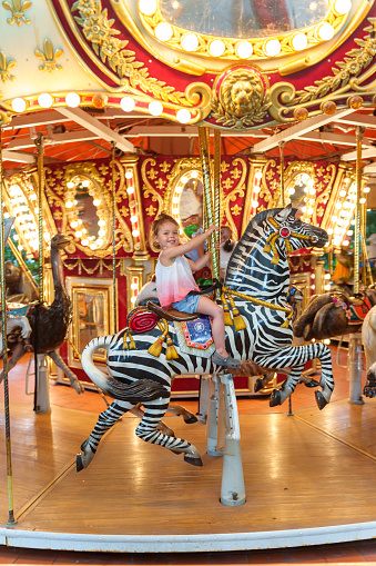 Two girls, cute little sisters riding together on a carousel in amusement park.