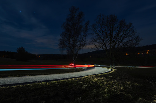 Light trails from car riding in curve asphalt street at night. Transportation background, long exposure