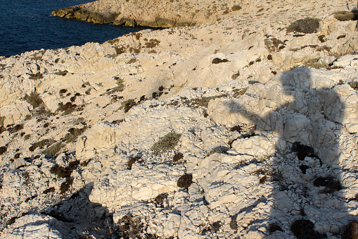 Shadow of the photographer on the white limestone surface of rocks. Marseille, Les Goudes, France.