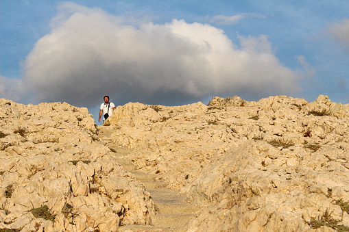 Marseille, France, 09 25 2023 : Man walking on a path in the Calanques of Marseille, Les Goudes, France. Golden evening light. blue sky, clouds.