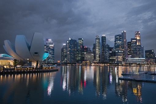 Singapore - December 28th, 2023: Singapore Urban Cityscape - Skyline at Marina Bay after Sunset under thick Thunderstorm Cloudscape. View over the glowing Singapore Waterfront Modern Skyscrapers and light reflections under dark blue twilight skyscape. Singapore, Southeast Asia, Asia