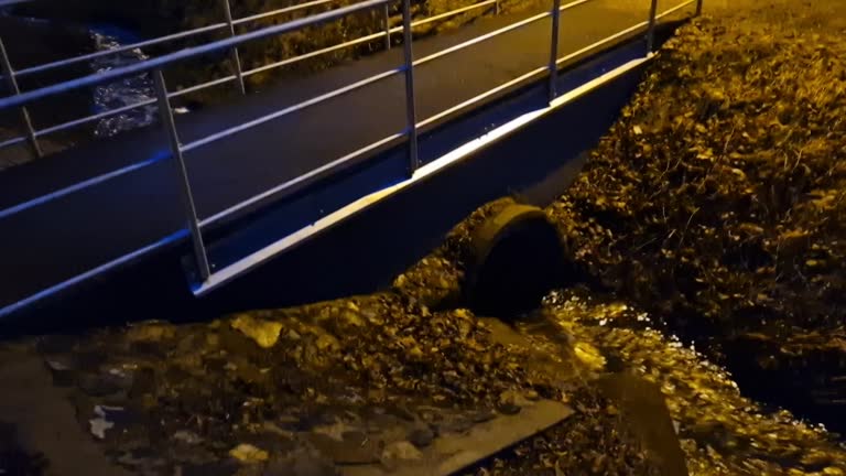 newly renovated bridge in the park over a small stream. concrete structures with a pipe passing through the flow lines. asphalt surface, metal sheet zinc drip tray. pipe railings, lawn, garden, cycle