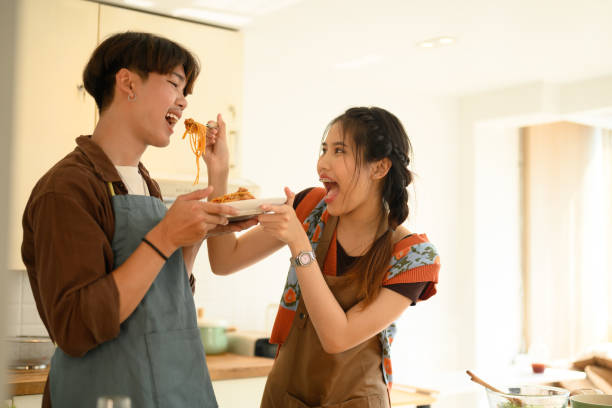 istock Playful young woman feeding her husband with spaghetti in kitchen, spending time together at home 2034670018