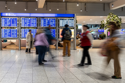 Frankfurt Airport, Germany - February 12, 2024: people in motion blur walking along in front of a departure scoreboard