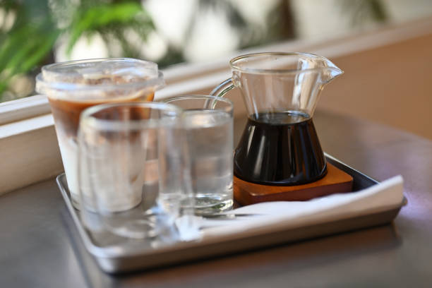 Freshly iced coffee and brewed coffee in a small pitcher with an empty and water glasses on the tray in the cafe.