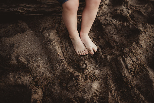 Little boy sitting on a log with his feet in the wet sand