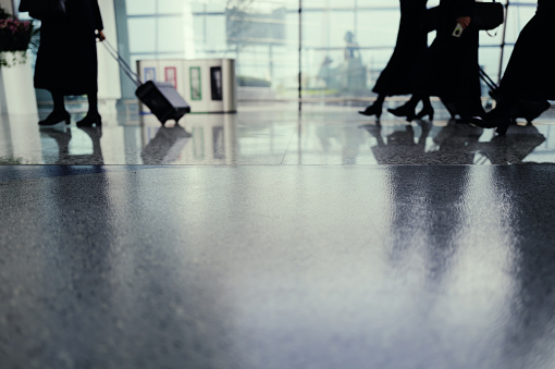 The focus is on the floor of the airport lounge with a blurred background depicting several flight attendants pulling luggage through the lounge, heading towards the parked aircraft. Captured with the Leica Q3.