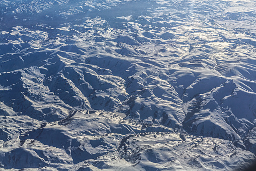 From the vantage point of an airplane, the majestic landscape below reveals snow-capped mountains stretching as far as the eye can see.