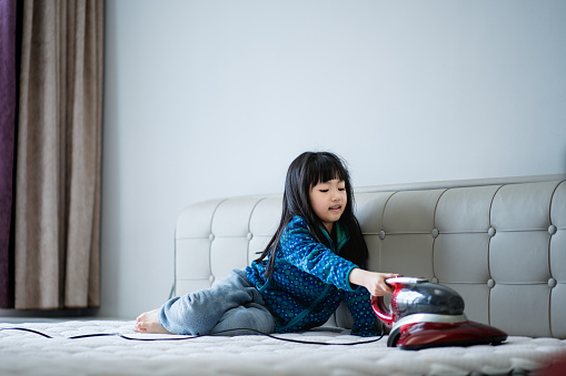 The girl is holding a vacuum cleaner to dust the bed,Girls do household chores at home