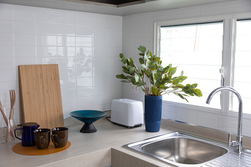 Bread toaster on kitchen worktop with kitchen utensils and tiled walls.