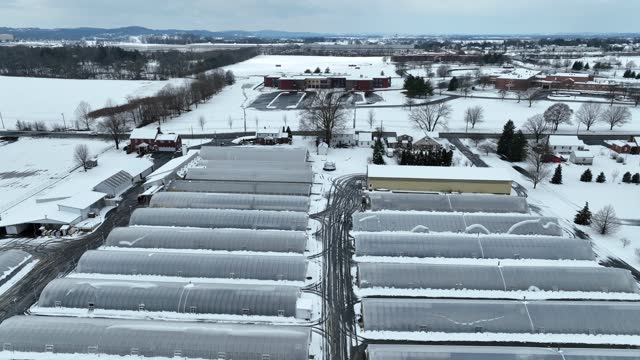 Rising aerial shot of greenhouses covered in snow. United States agriculture theme.