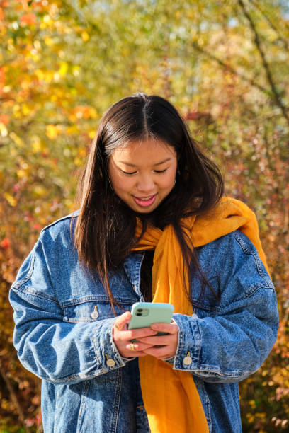 istock Young Chinese woman smiling and using the phone in a park in fall. 2034854493