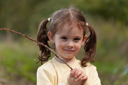 Little girl with long hair holding a branch in her hand, outdoors