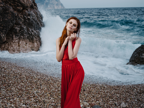 woman in red dress posing shore rocks ocean nature. High quality photo