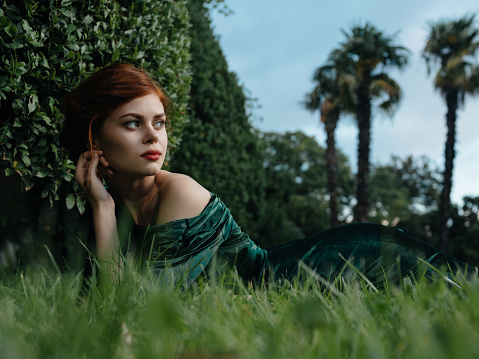 pretty woman in green dress lies on the grass in the fantasy garden. High quality photo