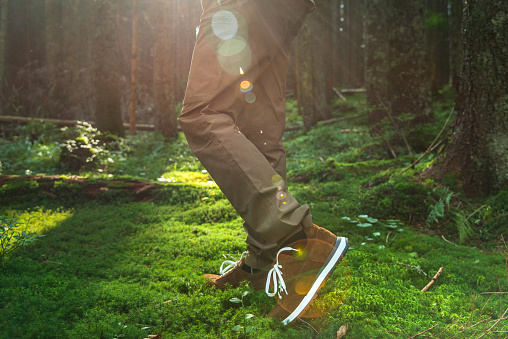 Young male walking on moss wearing brown suede sneakers in the dense forest