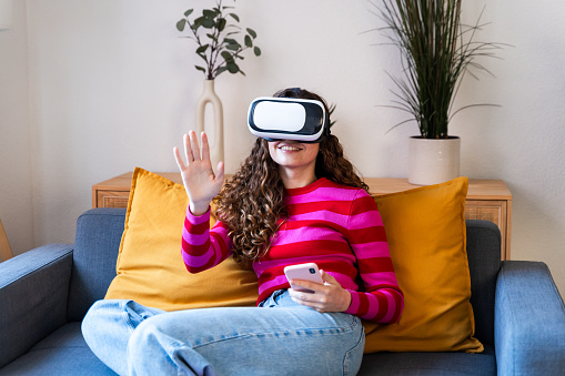 Smiling woman sitting on couch using VR and smartphone