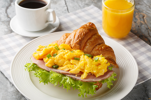 Healthy Breakfast Croissant with Scrambled Eggs and Ham Served with Orange Juice and Coffee Closeup on a Marble Table. Horizontal