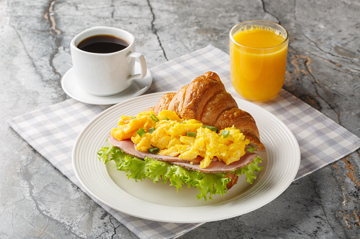 Scrambled egg sandwich with ham, green onions and lettuce served with orange juice and coffee close-up on a marble table. Horizontal