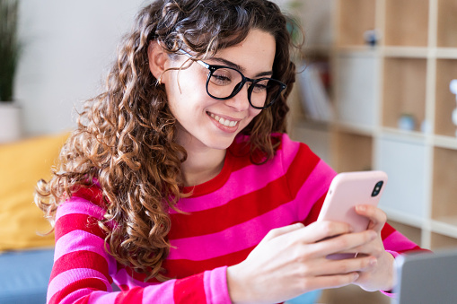 Curly-haired woman browsing smartphone with a smile at home