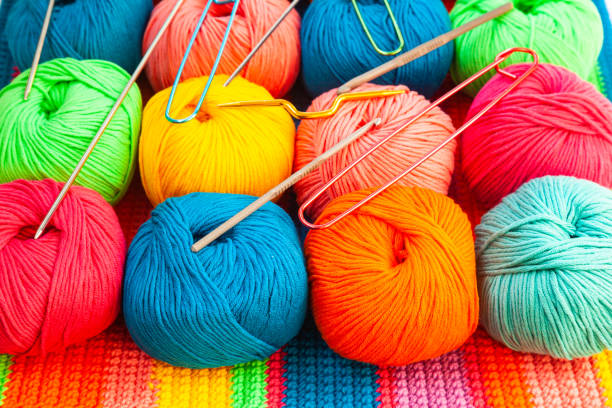 istock All for hand knitting. Knitted multi-colored handmade fabric with balls of multi-colored threads, pins and various knitting needles on it. 2035048829